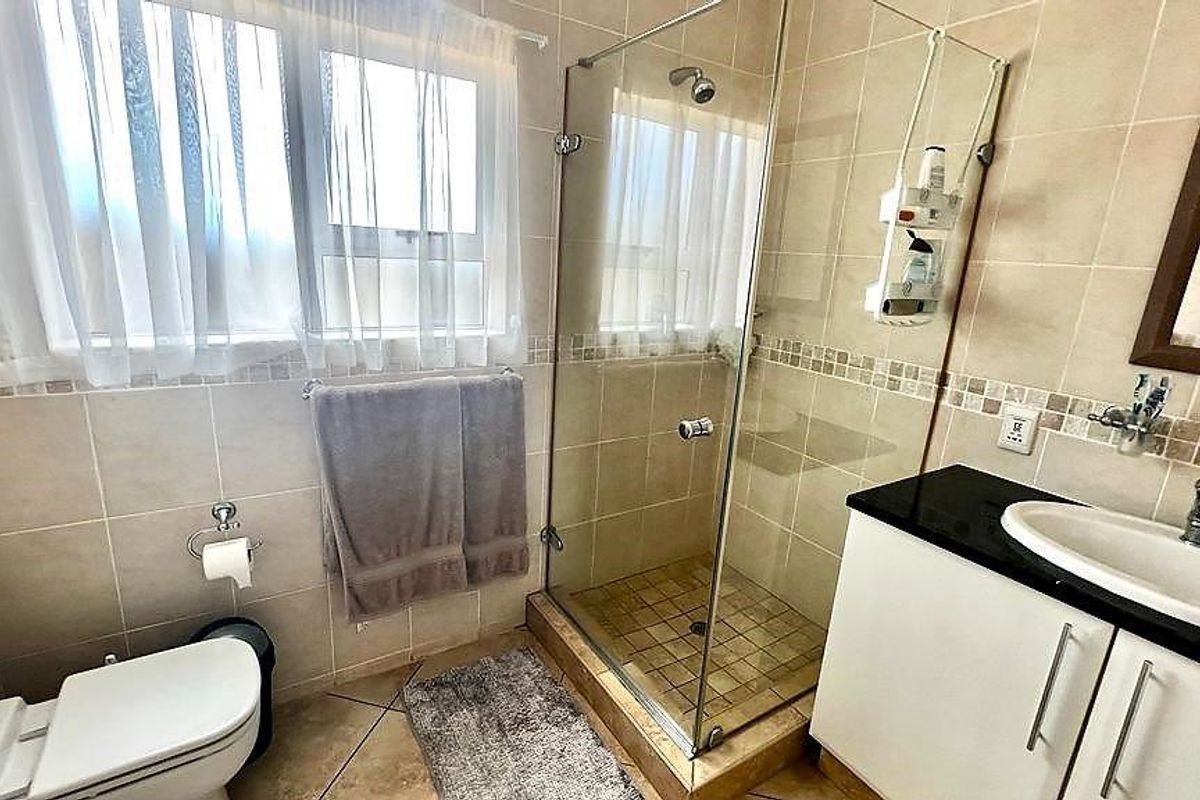 A functional bathroom featuring a glass-enclosed shower, vanity cabinet with basin, and neutral ceramic tiling throughout.