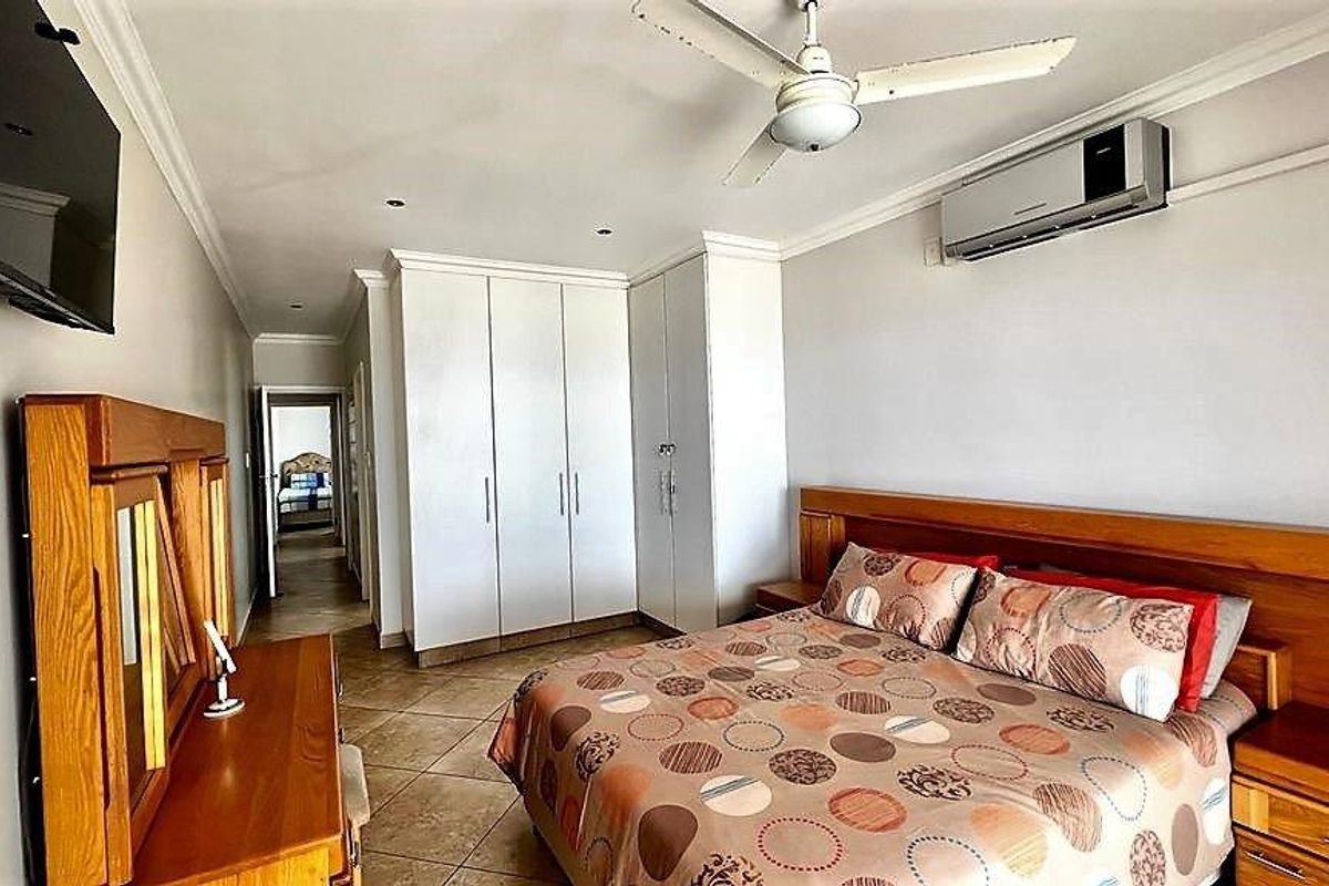 Spacious bedroom featuring built-in cupboards, tiled flooring, a ceiling fan, and a wall-mounted air conditioning unit.