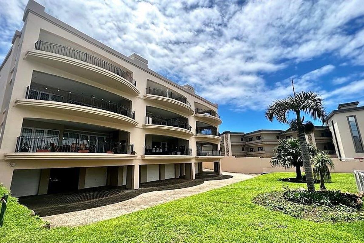 Rear view of a multi-story apartment complex featuring private balconies with wrought iron railings, ground-level garage access, and a well-maintained lawn.
