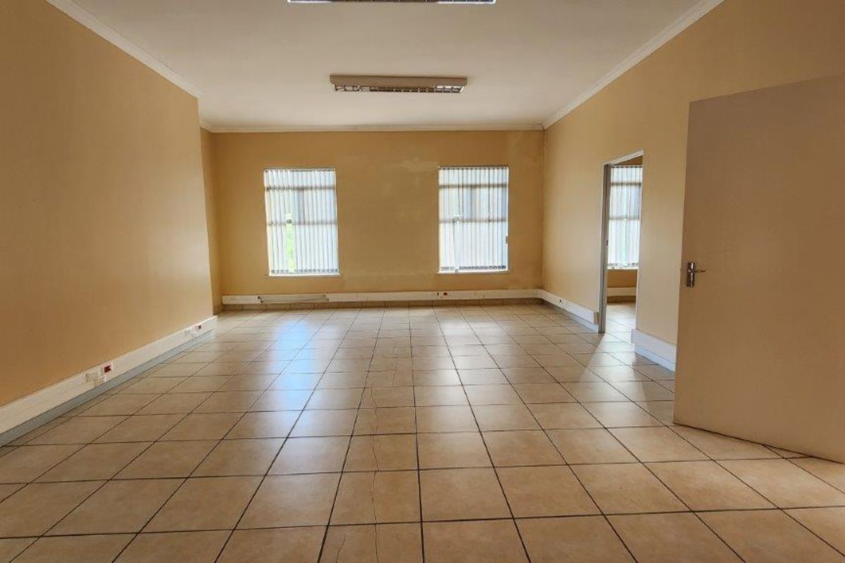 A vacant commercial office space featuring tiled flooring, fluorescent lighting, and vertical blinds, offering a blank canvas for professional use.