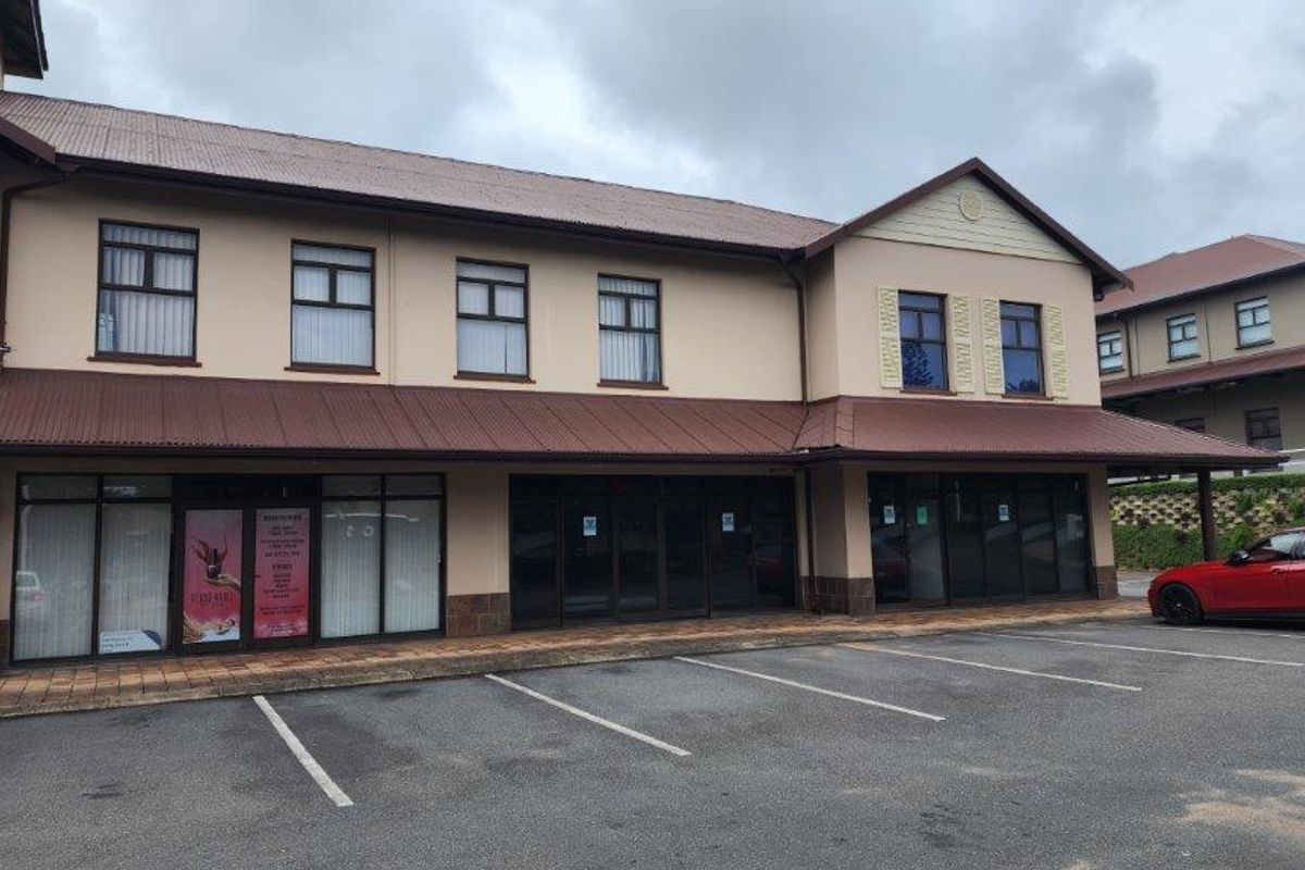 Front elevation of a commercial building featuring a metal roof, large glass storefronts, and an adjacent paved parking area.