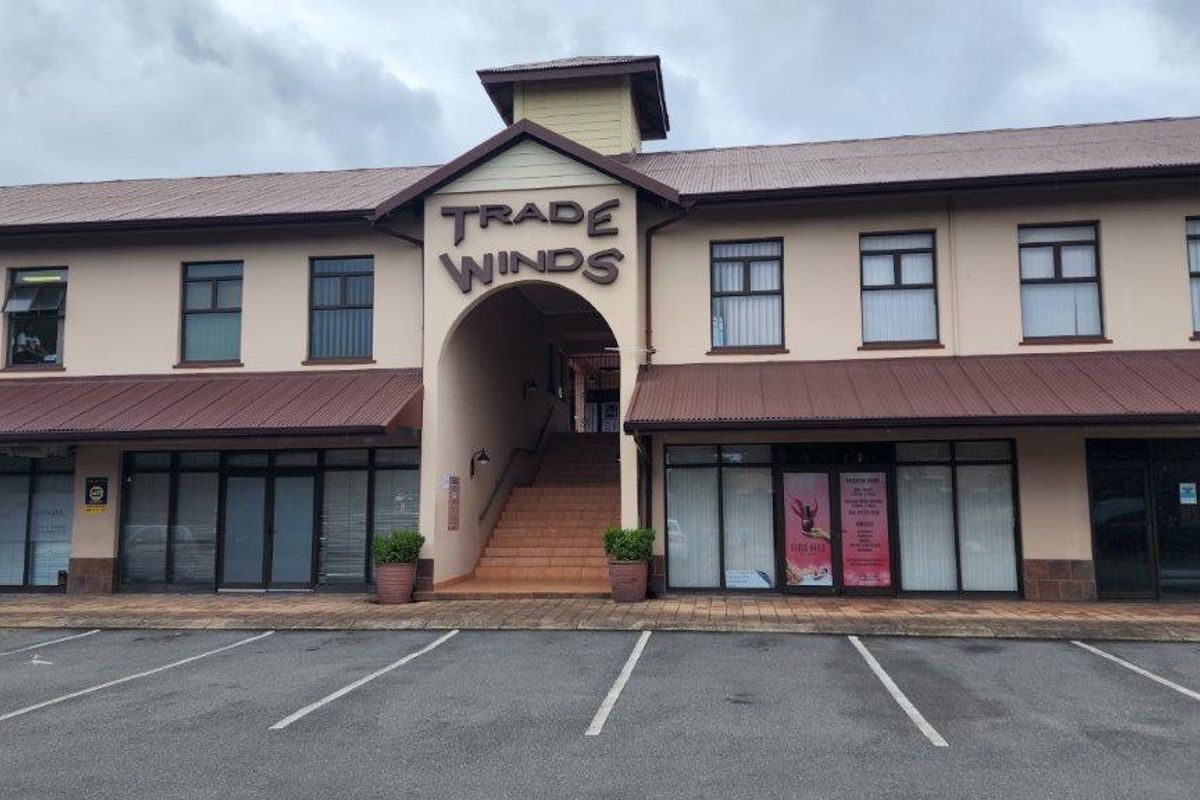 Front elevation of the Trade Winds commercial building featuring a central staircase, glass storefronts, and paved parking area.