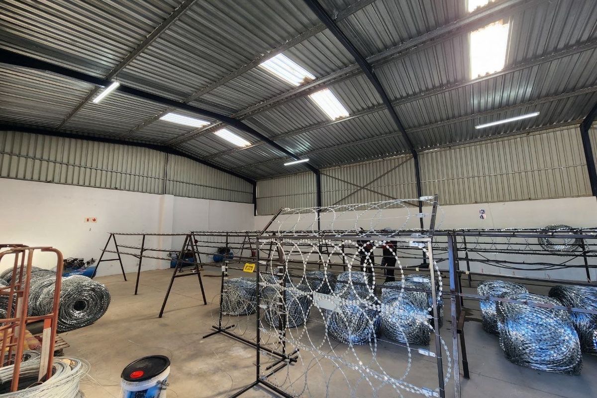Industrial utility space featuring high corrugated metal ceilings, exposed steel trusses, and durable concrete flooring, suitable for storage or manufacturing operations.