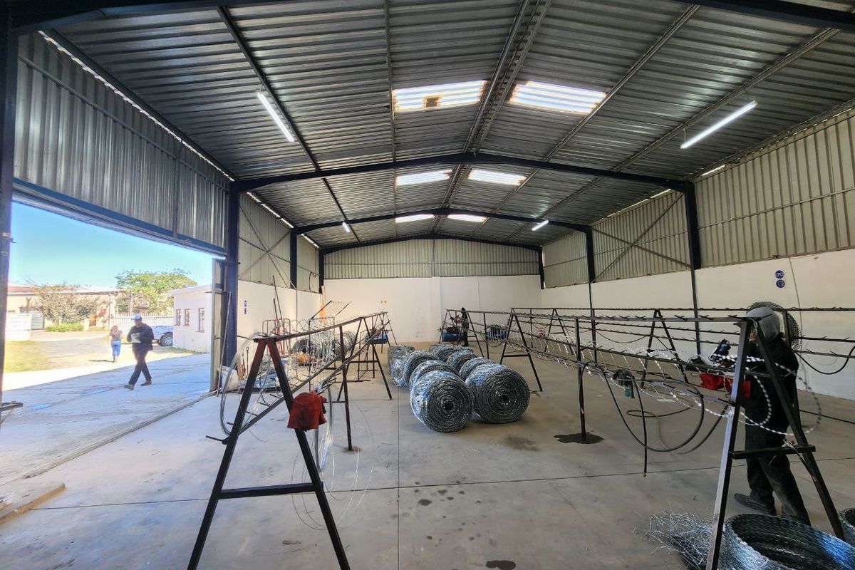 Spacious industrial warehouse unit featuring high ceilings, corrugated metal roofing, concrete flooring, and a large sliding access door.