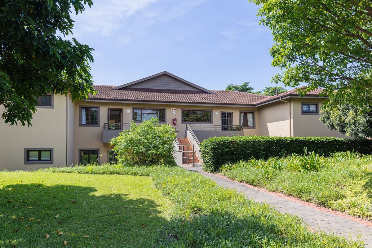 A well-maintained exterior view of an apartment complex featuring a tiled roof, paved walkway, and landscaped garden area.