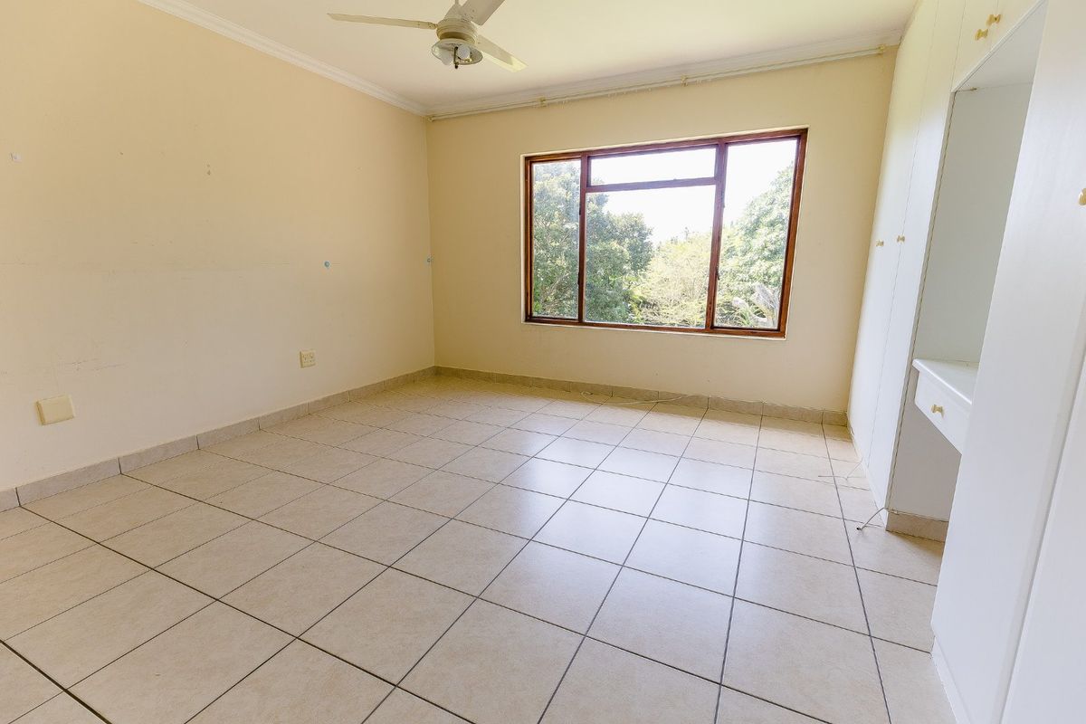 A spacious, empty bedroom featuring tiled flooring, built-in cupboards, and a ceiling fan, offering a blank canvas for personalization.
