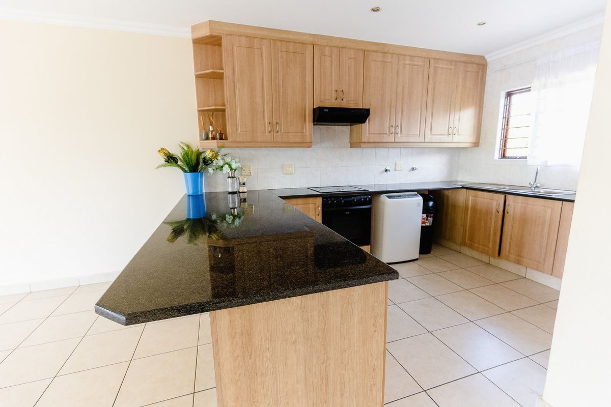 A functional kitchen featuring light wood cabinetry, dark granite countertops, a breakfast bar, and tiled flooring.