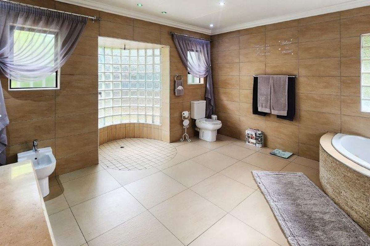 Spacious bathroom featuring a built-in bathtub, bidet, toilet, and distinctive glass block wall with neutral floor-to-ceiling tiling.