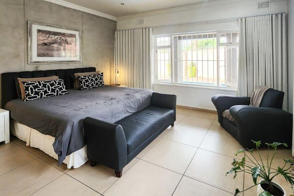 Spacious bedroom featuring large format floor tiles, a concrete feature wall, and large windows fitted with security bars and full-length curtains.