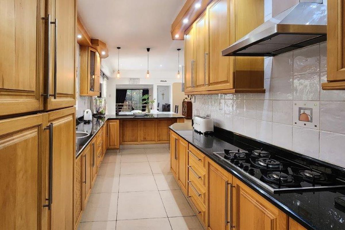 Spacious kitchen featuring extensive wooden cabinetry, granite countertops, a gas hob with extractor fan, and neutral tiled flooring.