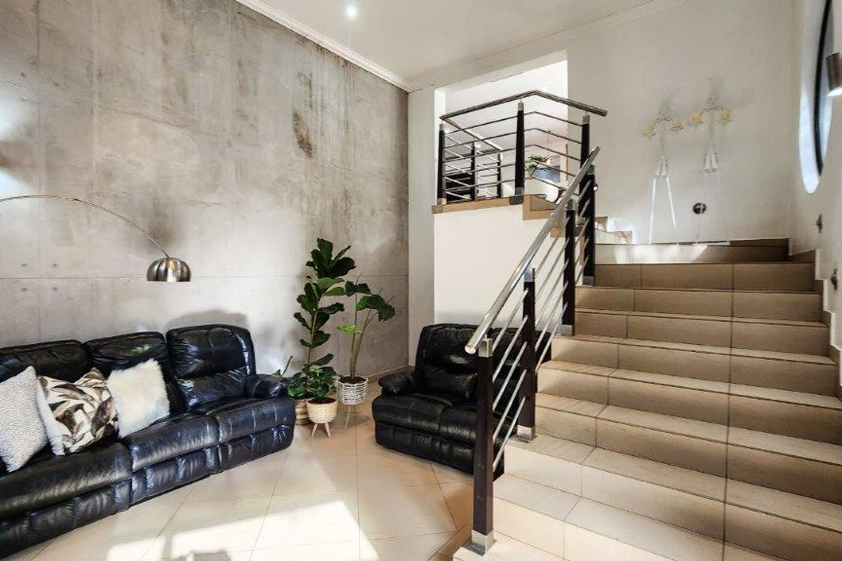Spacious living area featuring a striking exposed concrete feature wall and a tiled staircase with a modern stainless steel and timber balustrade.