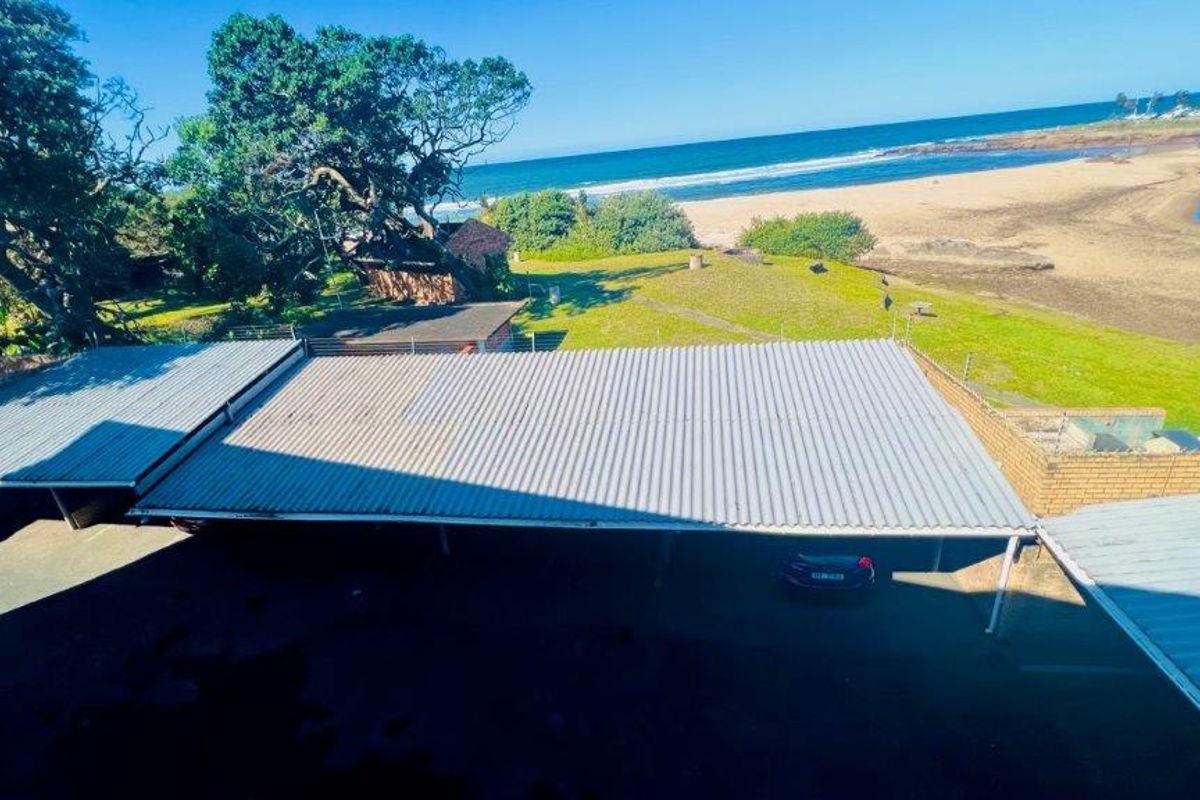 Aerial view of the apartment complex parking area featuring a corrugated metal carport structure with direct proximity to the beach and coastline.