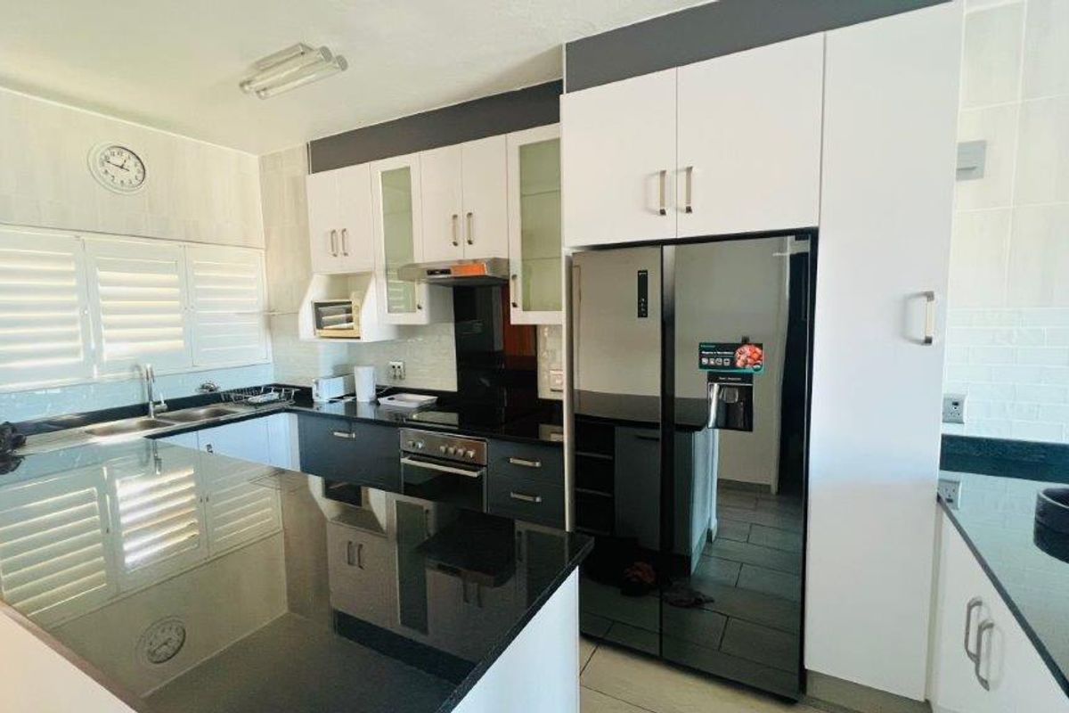 Modern kitchen featuring sleek white and dark cabinetry, granite countertops, integrated appliances, and stylish shutter blinds for a clean, functional workspace.
