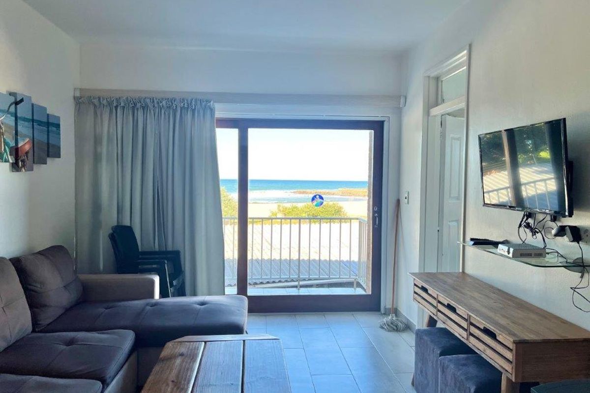 A living room featuring tiled flooring and a large sliding glass door that opens onto a balcony with ocean views.