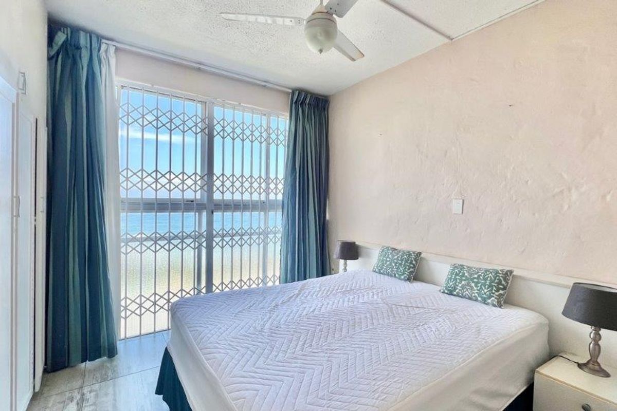 Bedroom featuring tiled flooring, a ceiling fan, and built-in wardrobe, with a security gate providing access to a sea view.