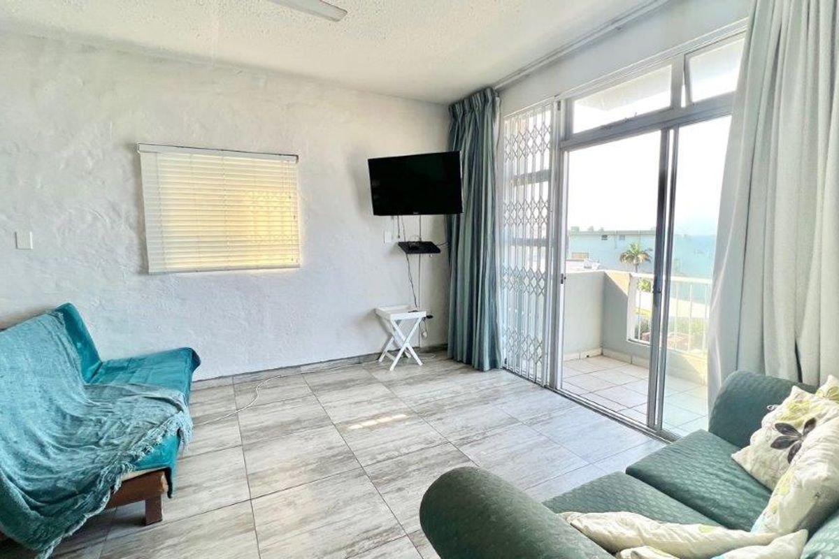 A living room featuring tiled flooring, textured walls, and a sliding glass door leading to a balcony with security gate access.
