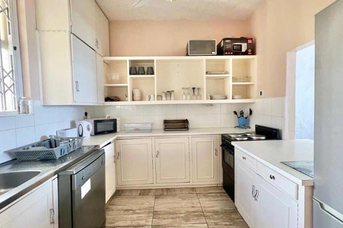 A functional kitchen featuring white built-in cabinetry, tiled backsplash, stainless steel sink, and tiled flooring, offering a practical layout for daily meal preparation.