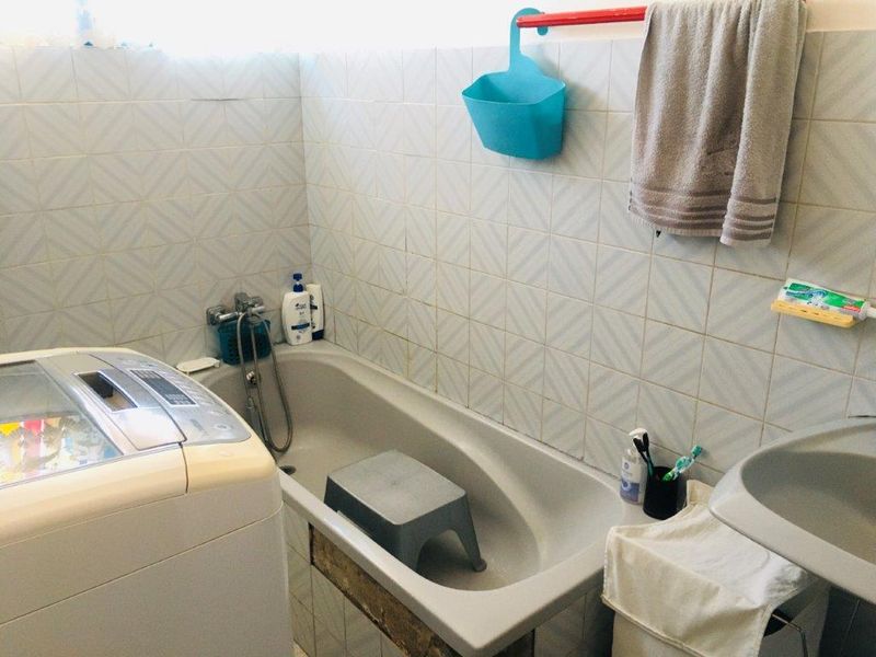 A functional bathroom featuring a bathtub with a handheld shower attachment, wall tiling, and a basin, showing signs of wear and dated finishes.