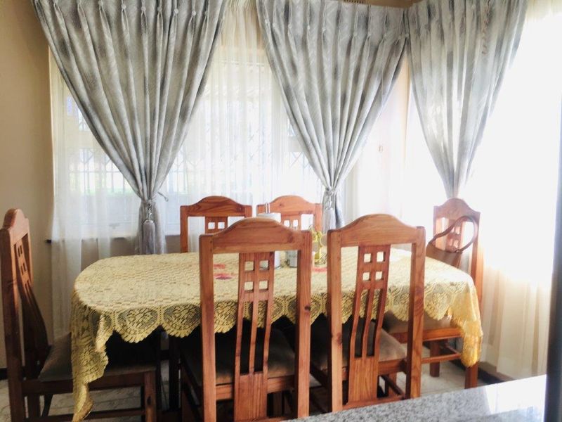 A dining room area featuring large windows with security bars and fitted curtain rails, providing natural light to the space.