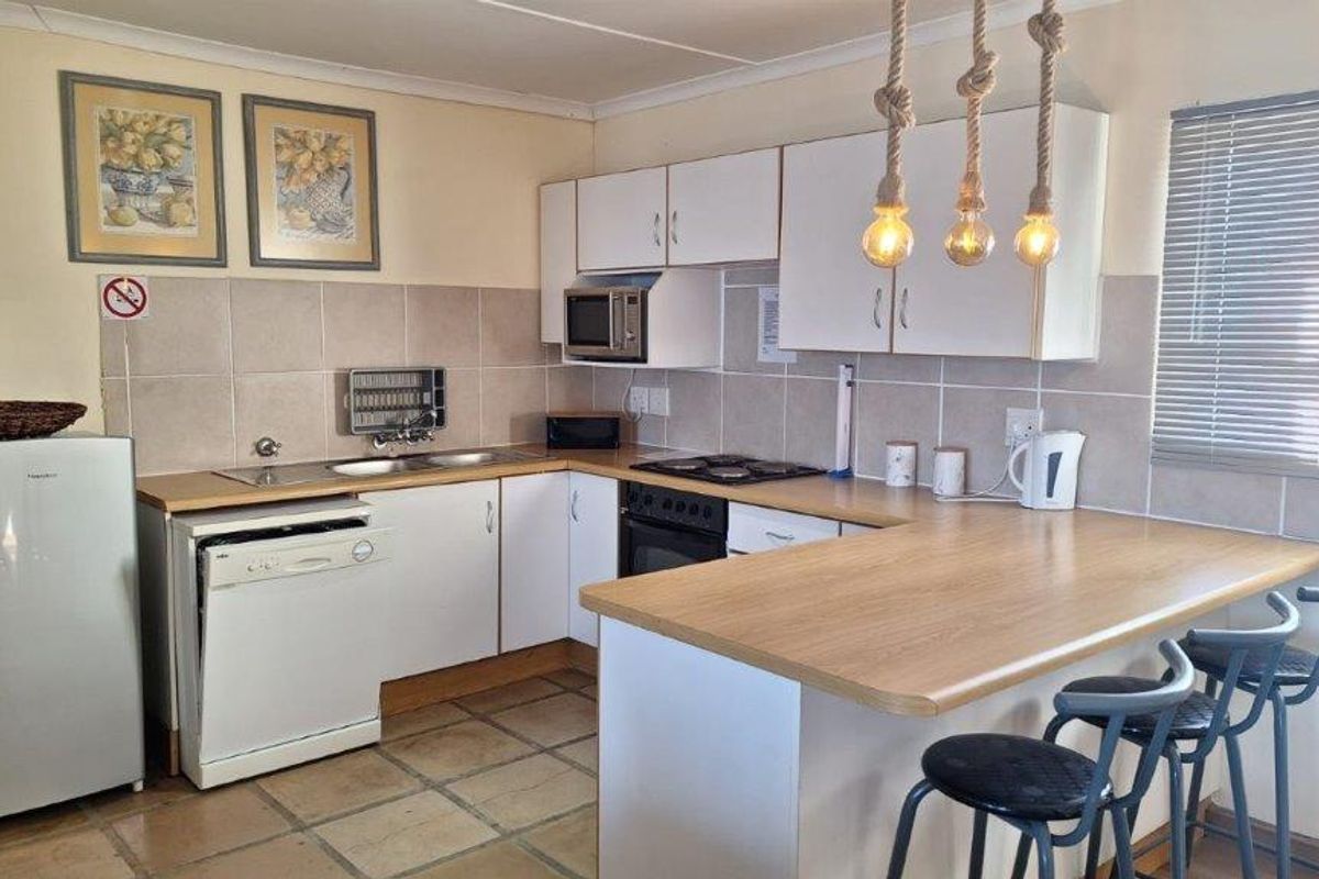Functional kitchen featuring white cabinetry, laminate countertops, tiled backsplash, built-in oven, hob, and a convenient breakfast bar for casual dining.