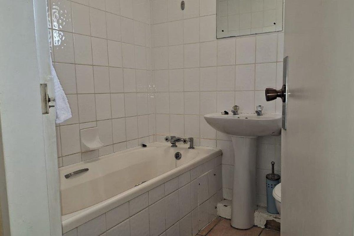 A dated bathroom featuring a pedestal basin and a built-in bathtub with white wall tiling, requiring cosmetic updates to improve its condition.