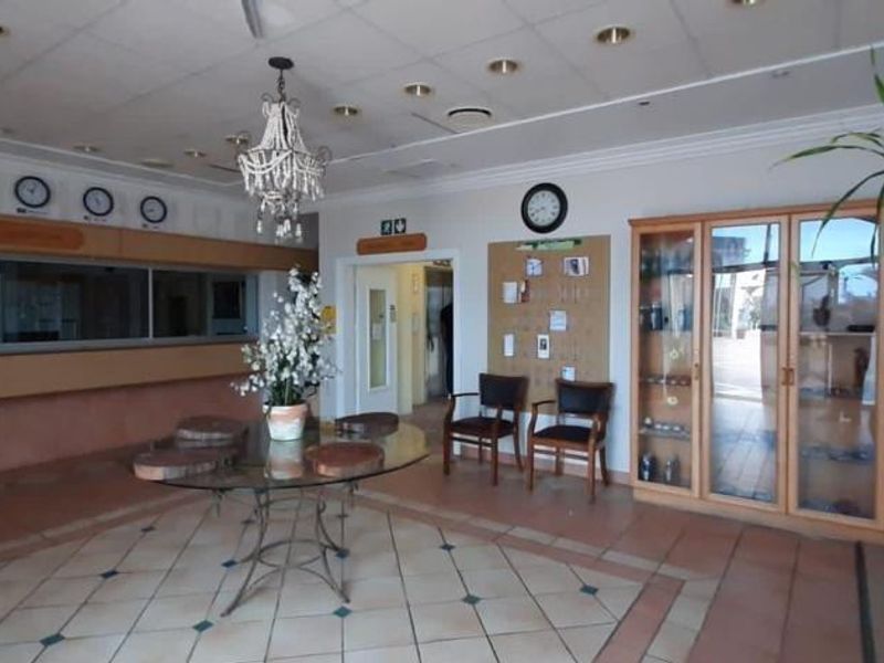 Spacious apartment building entrance lobby featuring a reception desk, built-in display cabinetry, and tiled flooring with a drop ceiling.