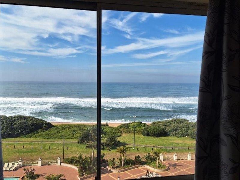A scenic view of the ocean and coastline captured through a large sliding glass door.