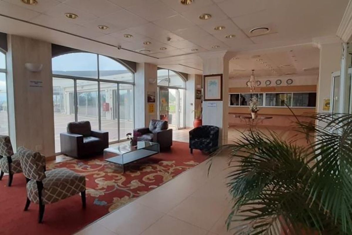Spacious apartment building entrance lobby featuring a reception area, large glass sliding doors, and tiled flooring.