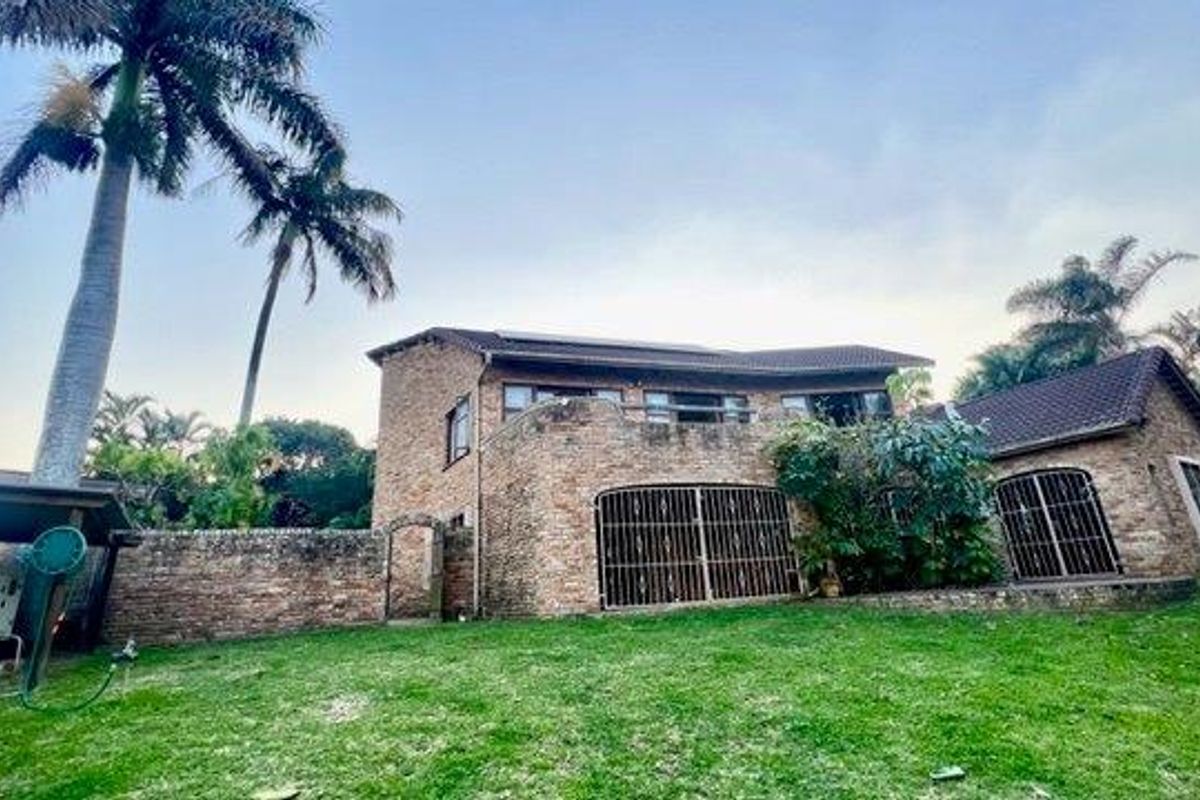 Rear view of a double-story face-brick house featuring a balcony, security gates, and solar panels set within a spacious garden.