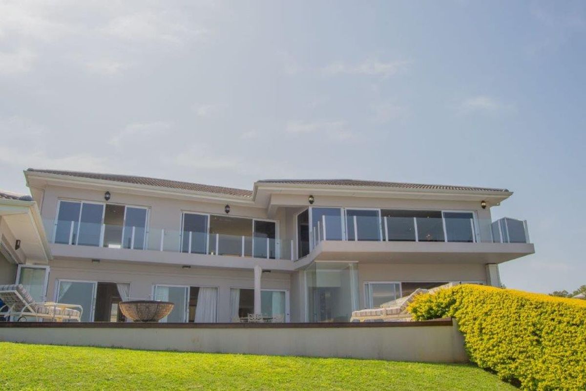 Rear elevation of a two-story residence featuring extensive glass sliding doors, upper-level balconies with glass balustrades, and a landscaped lawn area.