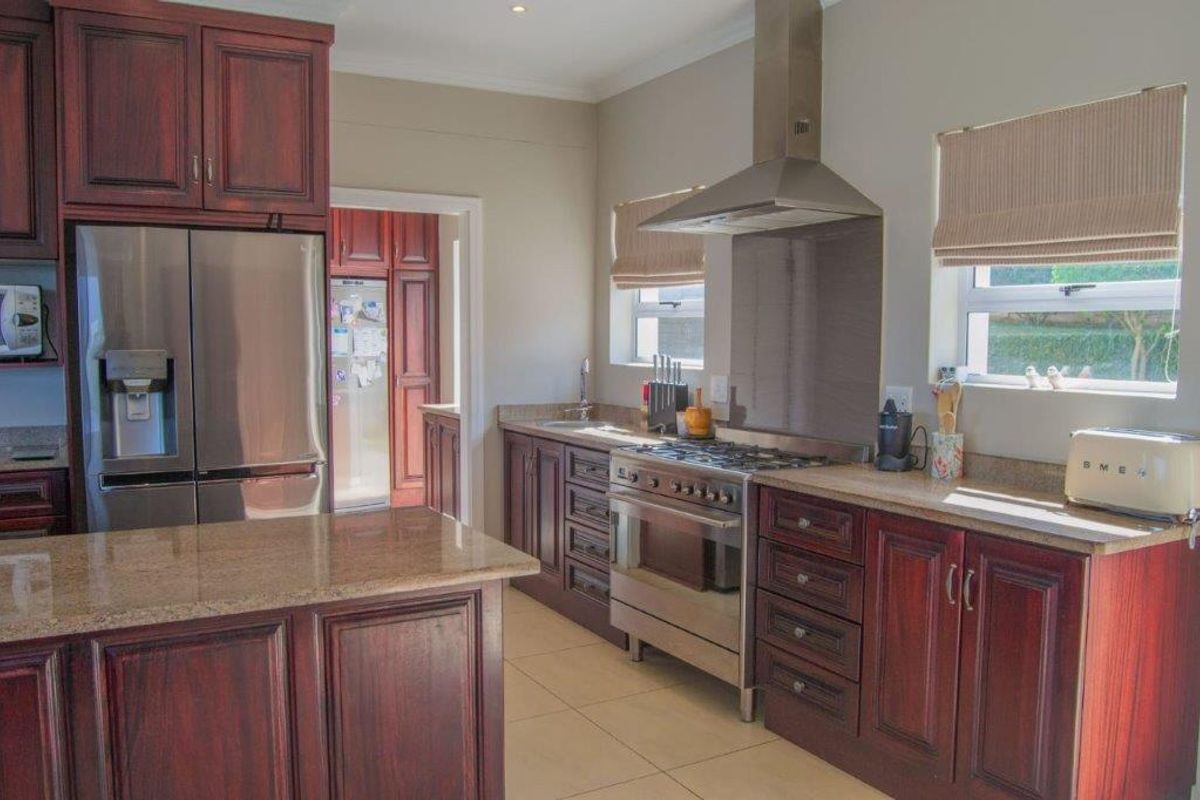 A well-appointed kitchen featuring dark wood cabinetry, granite countertops, stainless steel appliances, and a functional layout with an adjacent scullery area.