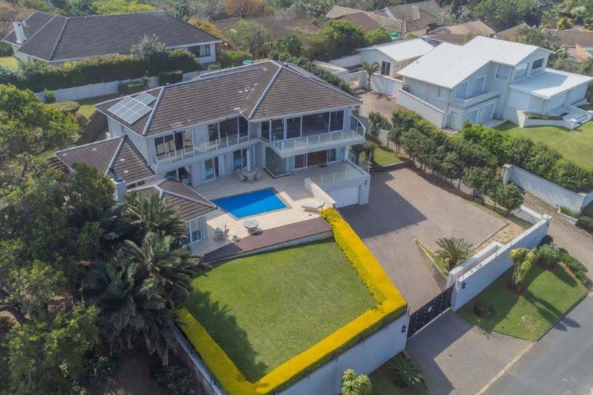 Aerial view of a large residential property featuring a swimming pool, paved driveway, solar panels, and landscaped garden areas.