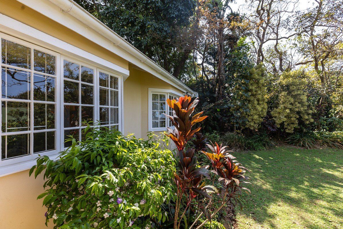A view of the rear exterior facade featuring white-framed casement windows and a bay window, set against a lush, mature garden.