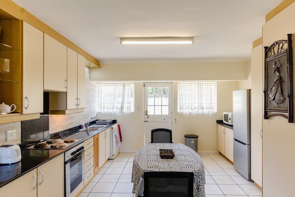 A functional kitchen featuring light-toned cabinetry, granite countertops, integrated oven and hob, and tiled flooring with direct access to the exterior.