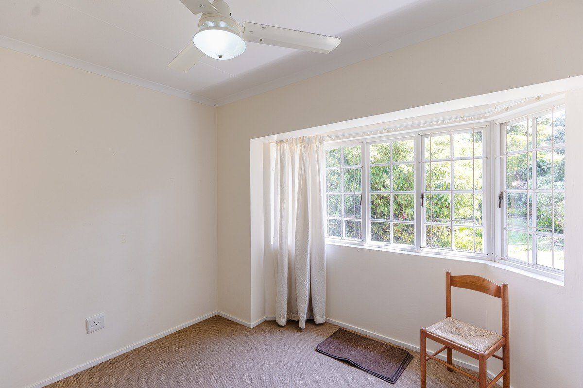 A bright, empty bedroom featuring a large bay window, neutral carpet flooring, and a ceiling fan, offering a blank canvas for personalization.