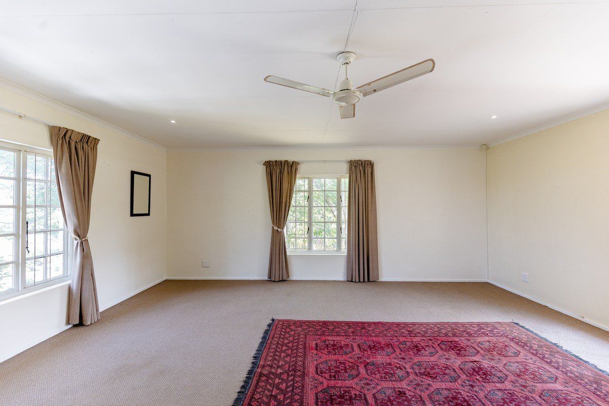 A spacious, light-filled living room featuring neutral carpeting, a ceiling fan, and large multi-pane windows, offering a blank canvas for interior design.