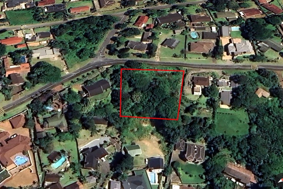 An aerial view of a vacant residential plot surrounded by established suburban housing and dense vegetation.