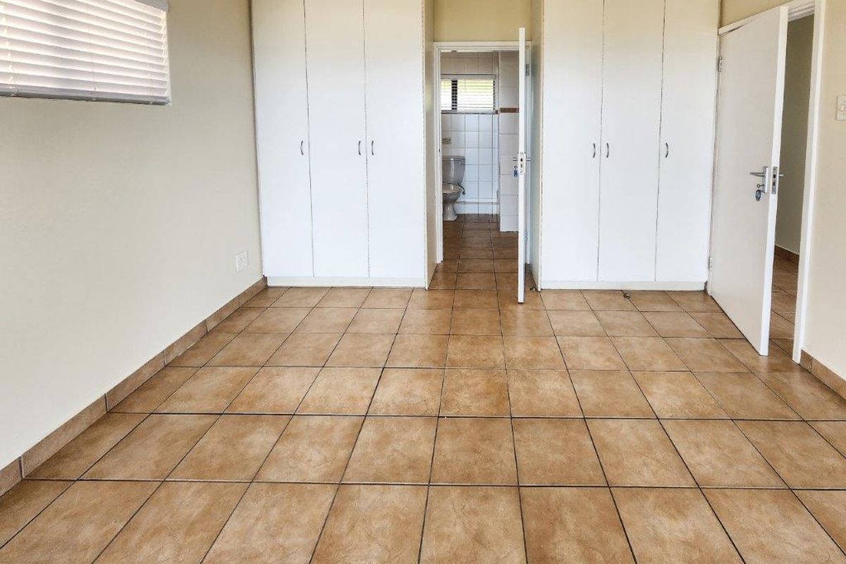 A spacious bedroom featuring built-in cupboards, tiled flooring, and direct access to an en-suite bathroom.