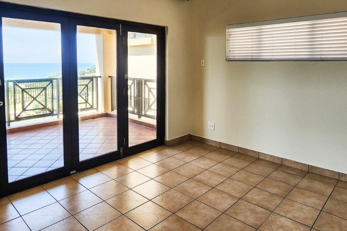 An empty living room featuring tiled flooring, large glass sliding doors leading to a balcony, and a window with fitted blinds.
