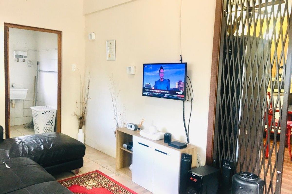 A living room area featuring tiled flooring and a security gate, with an adjacent view into a utility or laundry space.
