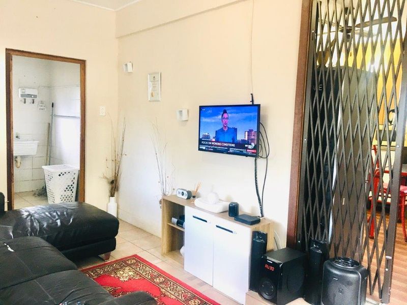 A living room area featuring tiled flooring and a security gate, with an adjacent view into a utility or laundry space.