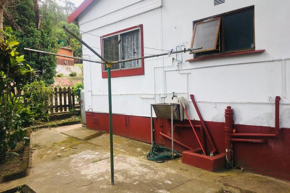 Rear exterior area featuring a concrete utility space, external plumbing, a stainless steel sink, and a rotary clothesline against the townhouse wall.