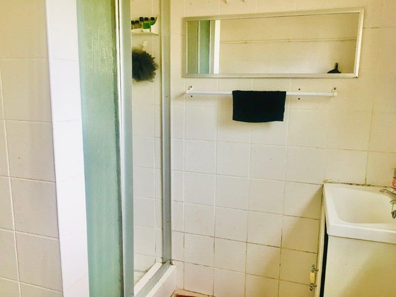 A dated bathroom featuring a shower enclosure, wall-mounted mirror, and a vanity basin with tiled walls.