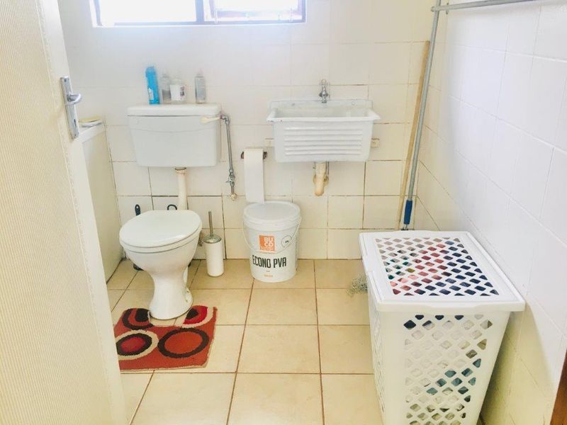 A functional laundry room featuring tiled walls and flooring, a utility sink, and a standard toilet, requiring cosmetic updates to improve its overall condition.