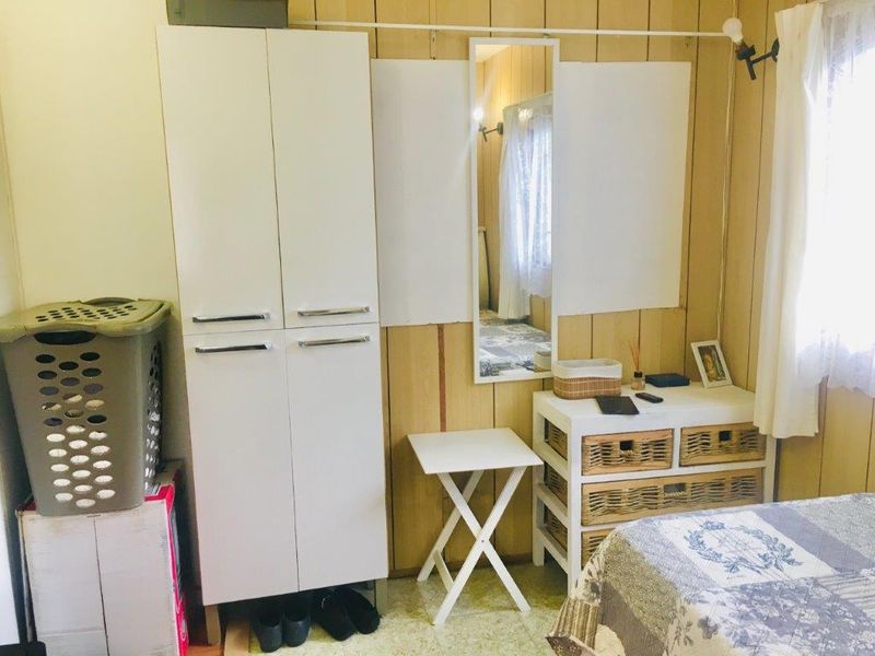A bedroom featuring timber wall paneling, a built-in wardrobe, and a wall-mounted mirror, offering a functional space with potential for modern updates.
