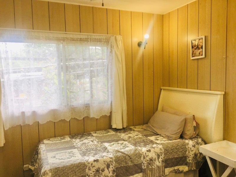 A bedroom featuring dated wood paneling walls and a wall-mounted light fixture, offering a cozy space with potential for modern updates.