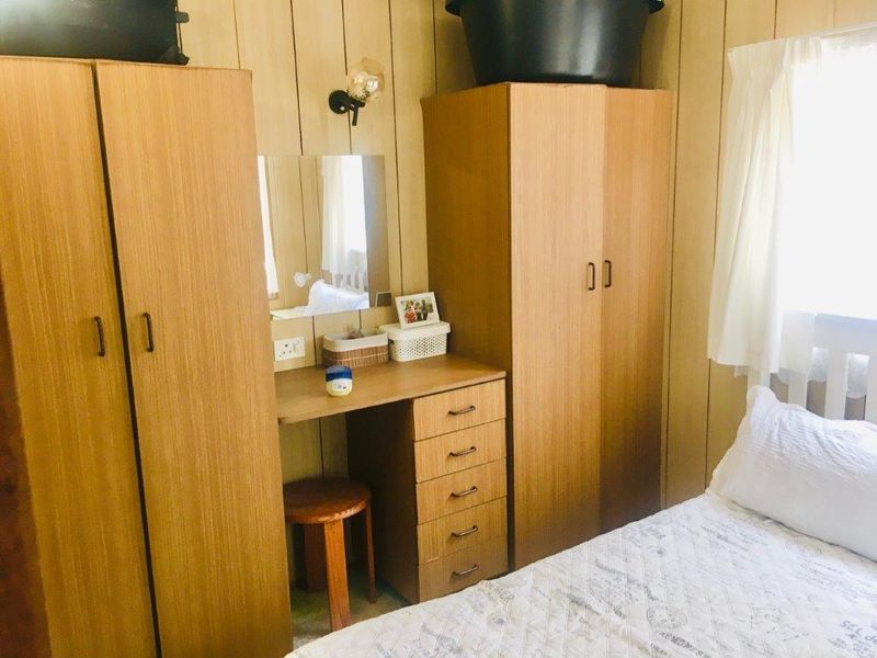 Bedroom featuring built-in wooden wardrobes and a matching vanity unit with wall-mounted lighting and wood-paneled walls.