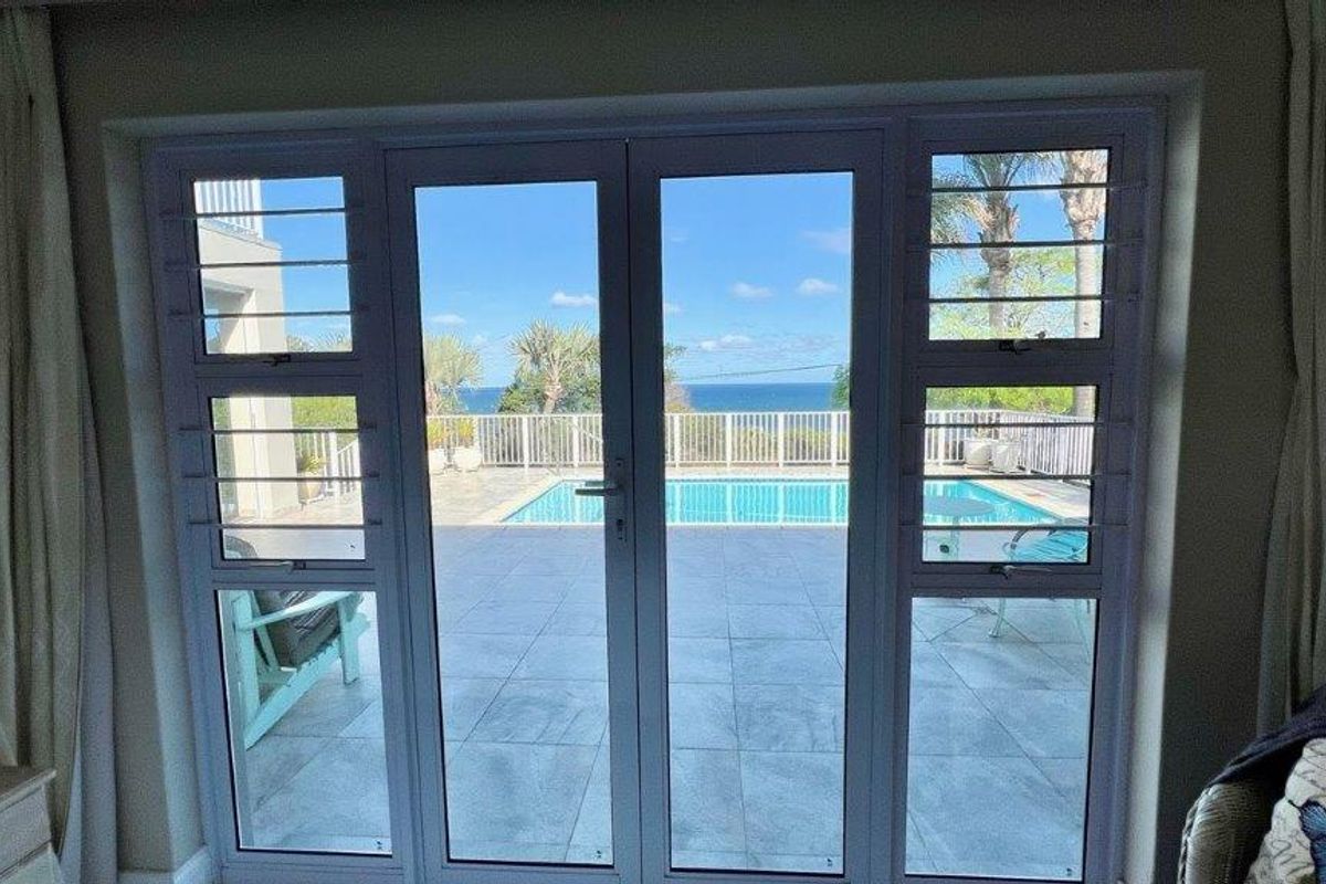 Living room featuring double glass doors opening onto a tiled patio with a swimming pool and ocean views.