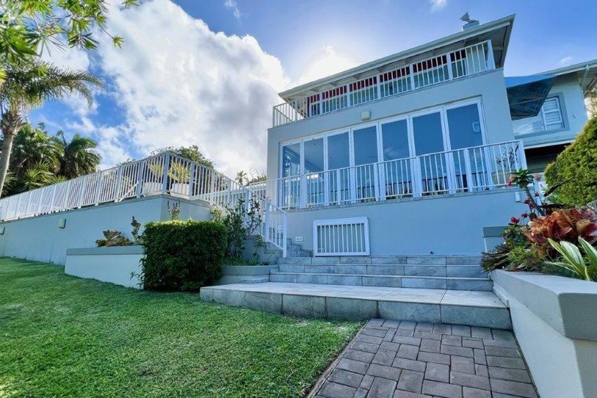 Rear view of the house featuring a raised patio, stone steps, metal railings, and large bi-fold doors leading to the upper level.