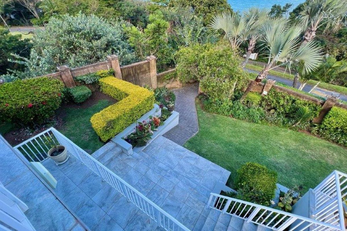 An elevated aerial view of a well-maintained garden featuring a stone-paved patio, brick pathways, and established landscaping with a retaining wall.